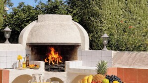 Forno a legna all'aperto con fuoco, circondato da un muro in piastrelle e un cesto di frutta.