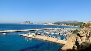 Una marina con imbarcazioni ormeggiate, una costa rocciosa e un cielo azzurro limpido.