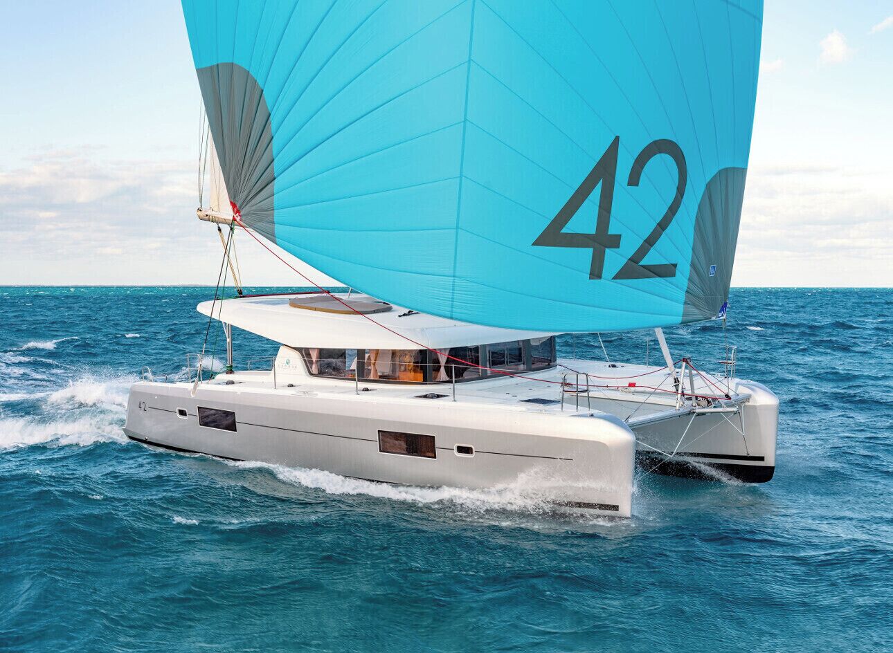 A catamaran with a large blue sail marked with the number 42, sailing on blue waters.