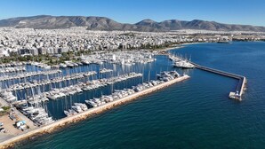 A marina with numerous boats docked, a long pier, and a cityscape with mountains in the background. - Sun-Kissed Sailing Adventure in Islas Sarónicas (Alimos)