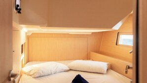 Cabine compacta e bem iluminada, com uma cama de solteiro, uma janela pequena e uma porta.