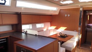 A compact kitchen with a central island, a dining area with a table and chairs, and a small seating nook with cushions. - Sun-Kissed Sailing Adventure in Islas Sarónicas (Alimos)