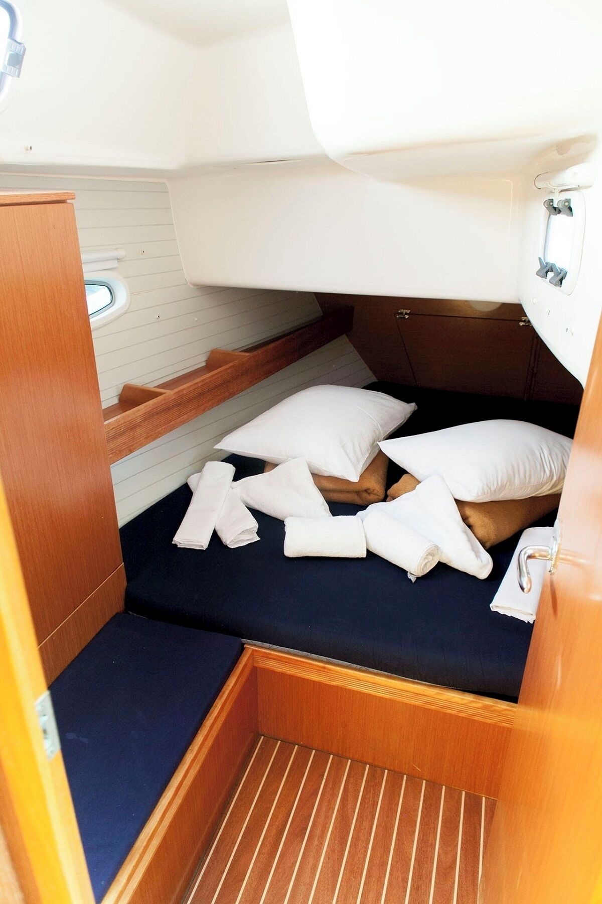 A compact boat cabin with a small bed, pillows, and neatly folded towels.