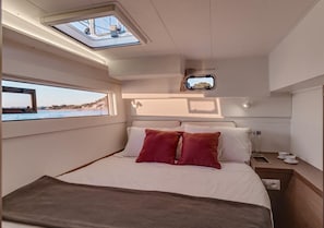 A bedroom with a bed, pillows, a bedside table, a window, and a skylight.