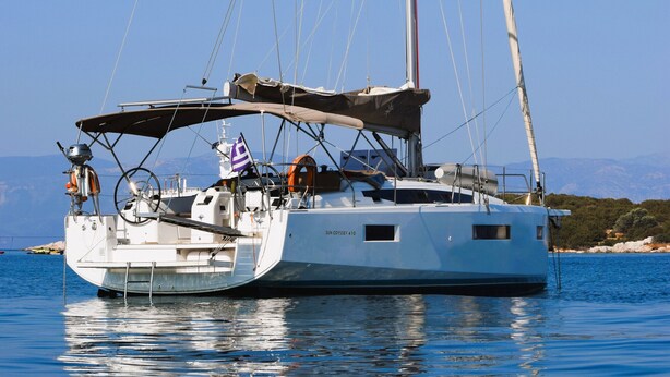 Un velero llamado SUN ODYSSEY 410 amarrado en aguas tranquilas, con cielo despejado y montañas a lo lejos.