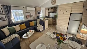A modern living room with a sofa, coffee table, and dining table set for a meal. - 5* 2025 - Siblu La Réserve sleeps 8, 2 bathrooms (Gastes)