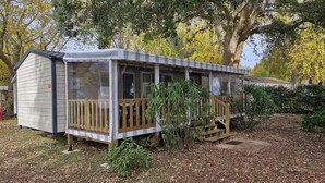 A small, single-story cabin with a porch, surrounded by trees and a grassy area. - 5* 2025 - Siblu La Réserve sleeps 8, 2 bathrooms (Gastes)