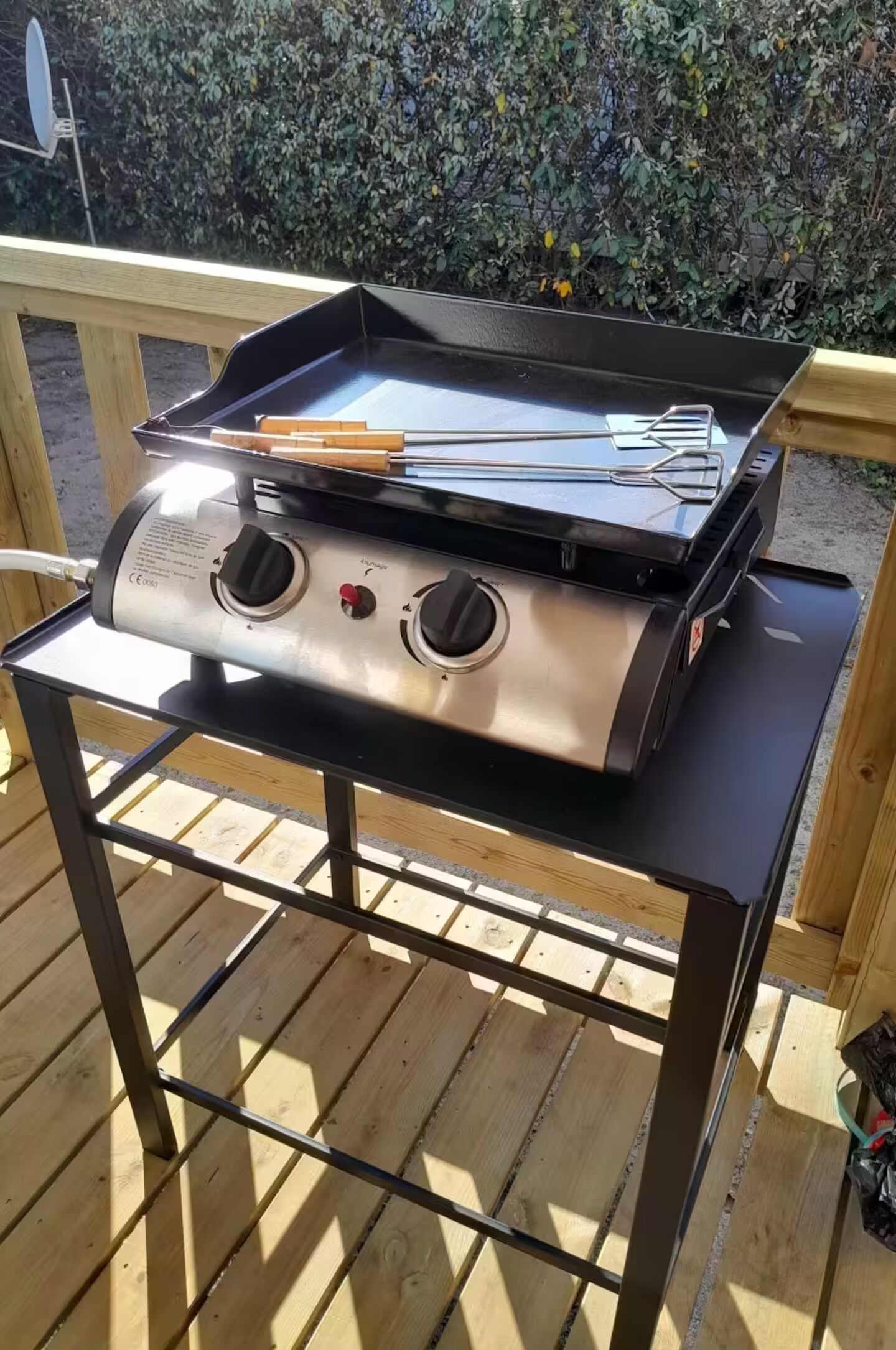 Ein tragbarer Gasgrill auf einer Holzterrasse, mit Metallgestell.