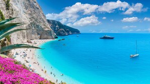 Ein Küstenstrand mit klarem türkisblauem Wasser, einer felsigen Klippe und einem Segelboot.