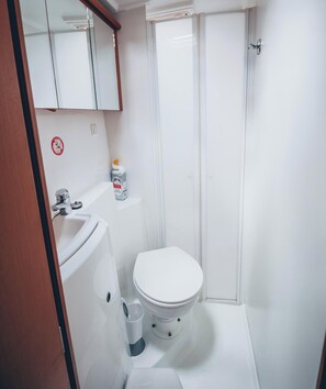 Une petite salle de bain avec un lavabo, des toilettes et une douche, le tout de couleur blanche.