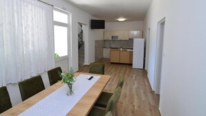 Een eetruimte met een lange tafel, stoelen, een vaas met bloemen en een keuken op de achtergrond.