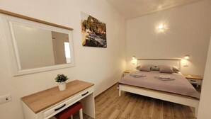 Een slaapkamer met een bed, nachtkastjes, een bureau, een stoel, een spiegel en een kleine plant.