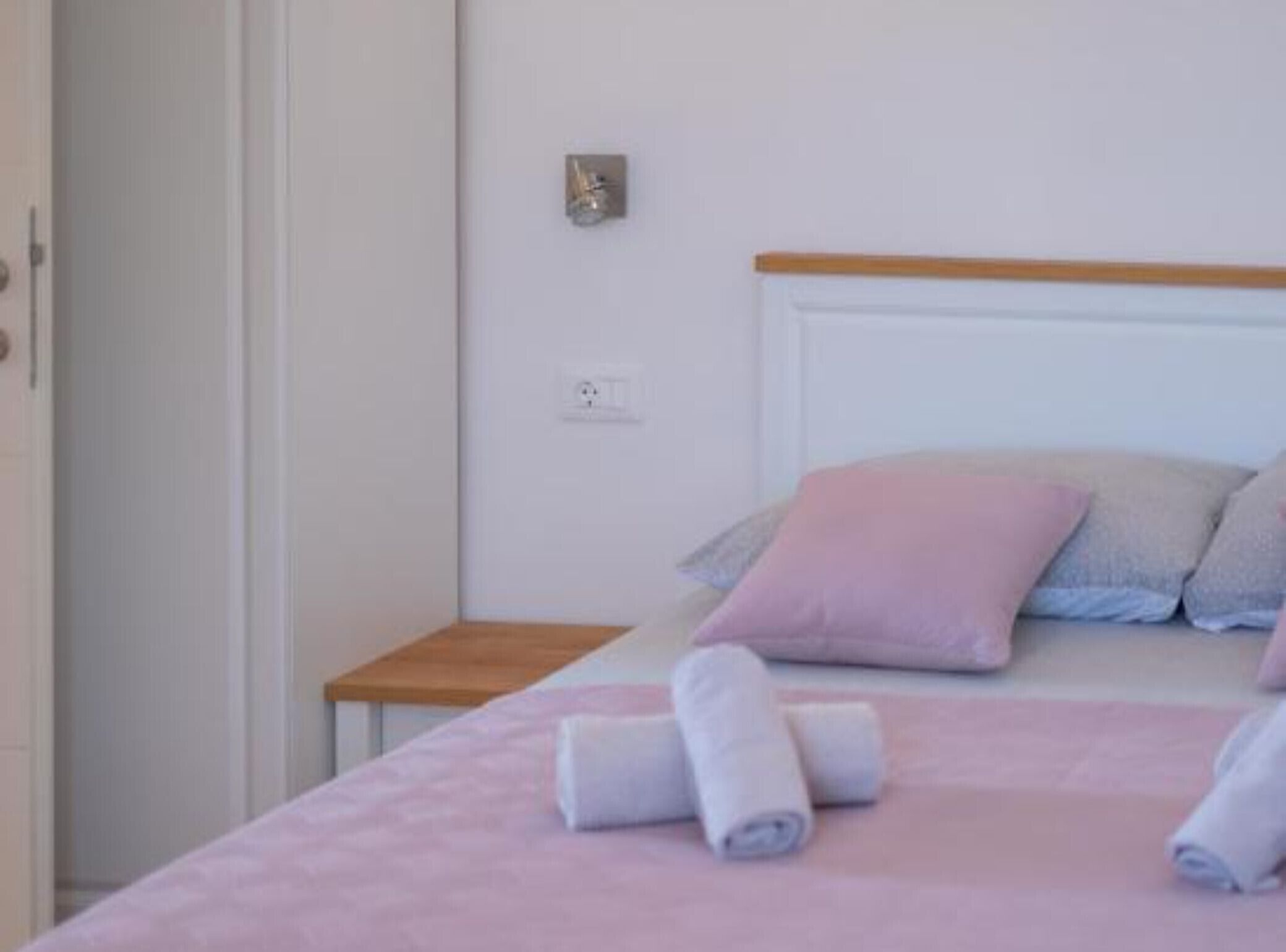 Een slaapkamer met een bed, kussens, een nachtkastje en een stopcontact.