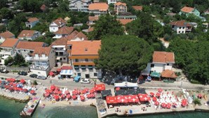 Luftaufnahme einer Küstenstadt mit Strandabschnitt, roten Sonnenschirmen und einem Steg.