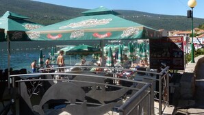 Un restaurant situé au bord de l’eau, avec une terrasse, des parasols verts et une vue sur la mer.