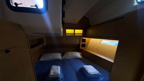 Ein kompakter, gut beleuchteter Innenraum mit einem Einzelbett, einem kleinen Fenster und einer Tür.