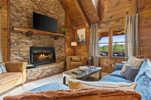 Ein gemütliches Blockhaus-Interieur mit Kamin, Holzwänden, einer Couch, einem Couchtisch und einem Fernseher.