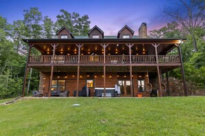 Eine Blockhütte mit Balkon, Sitzgelegenheit im Freien und einem Steinsschornstein.