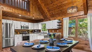 Interior de madeira com uma mesa de jantar posta para quatro, armários de cozinha e um lustre.
