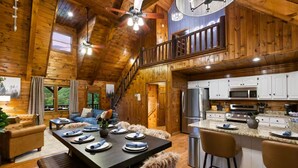 Uma cabana espaçosa com área de jantar, cozinha e escada para um andar superior.