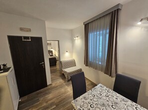 Habitación de hotel pequeña con cama, una mesita, dos sillas, un escritorio con computadora, una ventana con cortinas y una puerta.