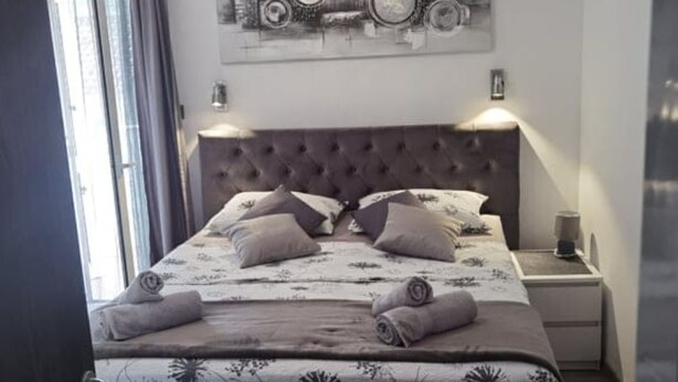 Un lit bien fait, avec une couvre-lit à motifs floraux et des oreillers, une tête de lit capitonnée, une horloge murale et une table de chevet avec une lampe.