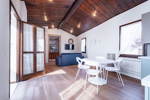 A modern interior with a wooden ceiling, a dining area with white chairs, a blue sofa, and a kitchen area with a window. - Attic Romance with Balcony (Verona)