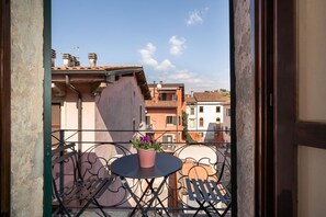 A balcony with a table and chairs, a potted plant, and a view of neighboring buildings. - Attic Romance with Balcony (Verona)