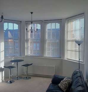 A room with three bar stools, a sofa, a radiator, and a chandelier. - Welcome to Highland Village 
We’re delighted to host you! (London)