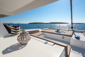 Ein Bootsdeck mit Sitzgelegenheiten, einer Laterne und Blick auf das Meer und das ferne Land.