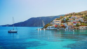 Uma vila costeira com edifícios numa encosta, barcos na água e um mar azul límpido.
