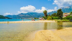 Uma praia com água cristalina, uma orla arenosa e montanhas ao fundo.