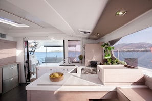 A modern kitchen with a view of the sea, a dining area with a view, and a seating area with a plant. - Sun-Kissed Sailing Adventure in the Stunning Islas Cícladas (Paros)