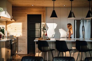 A modern kitchen with wooden cabinetry, a central island with bar stools, pendant lighting, and a stainless steel refrigerator. - Chalet Le Solem, Golf et Spa ! (Mont-Blanc)