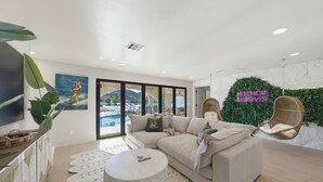 Una sala de estar moderna con un sofá, una mesa redonda de centro y un ventanal con vistas a una piscina y montañas.