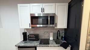 A compact kitchen with white cabinets, a built-in microwave, a toaster, and a refrigerator.