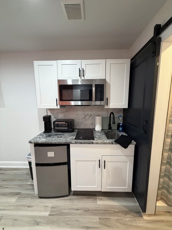 Una cocina compacta con armarios blancos, un microondas integrado, un tostador y un refrigerador.