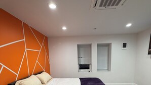 A modern bedroom with a bed, a nightstand, an air conditioning unit, and a window with blinds.