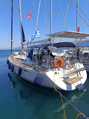 Un veler amarrat al port esportiu, amb diverses palenes i banderes, incloent-hi la bandera grega.