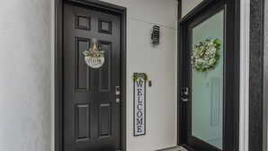 Une porte noire avec une pancarte indiquant «Bienvenue», une guirlande sur la porte vitrée et une petite plante accrochée au mur.