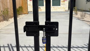 Une grille métallique fermée par un cadenas, une ligne jaune tracée au sol et, au fond, un bâtiment portant le numéro 4229.