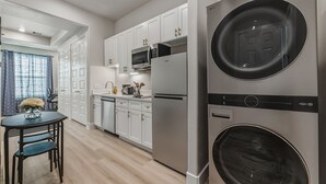 Une cuisine moderne avec des armoires blanches, des appareils en acier inoxydable et un lave-linge et un sèche-linge intégrés.