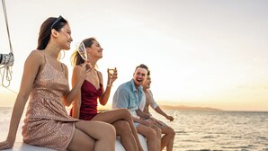 Eine Gruppe von Menschen auf einem Boot, mit Blick auf das Meer und einem Sonnenuntergang im Hintergrund.