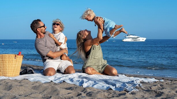 Eine Familie am Strand mit einem Picknickkorb und einem Boot im Hintergrund.