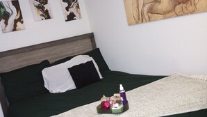 Uma cama com colcha verde, manta branca e mesa de cabeceira com artigos de higiene pessoal.