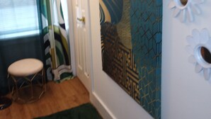 Quarto com uma pintura abstrata grande, um banquinho pequeno, tapete verde e elementos decorativos na parede.