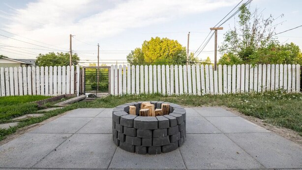 Een ronde vuurkuil met hout in het midden, omringd door een geplaveid terras.
