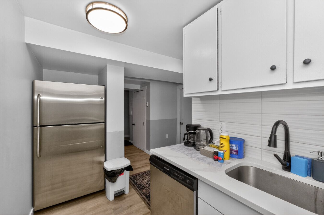 Cocina compacta con refrigerador de acero inoxidable, lavavajillas, pileta con grifo negro y cafetera.
