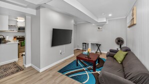 Een moderne woonkamer met een flatscreen televisie, een bank, een salontafel, en een keukenhoek met kastjes en een magnetron.