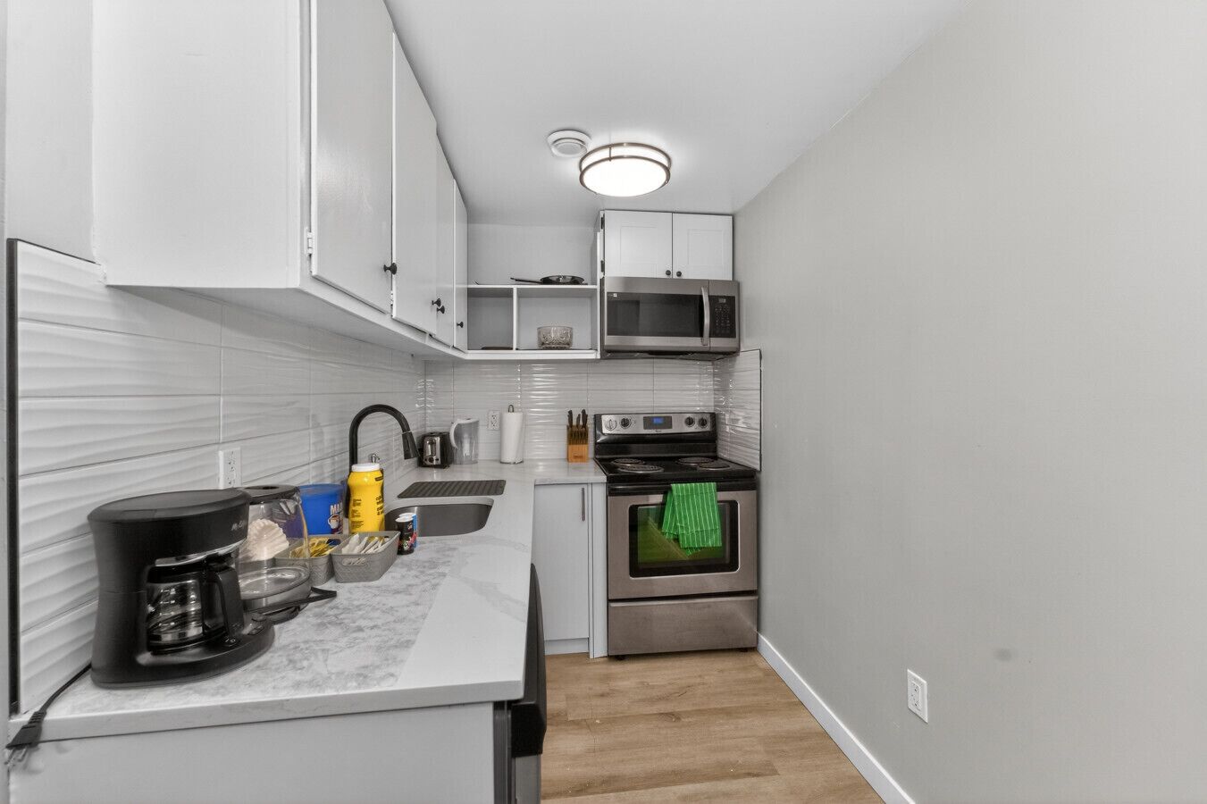 A compact kitchen with white cabinets, a microwave, a stove, and a coffee maker.